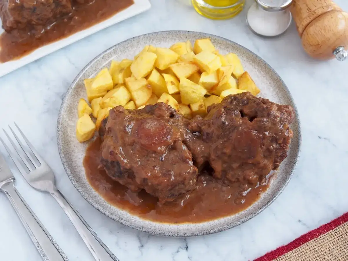 Dos trozos de rabo de ternera en salsa, acompañados de patatas fritas crujientes. Un plato tradicional listo para disfrutar.