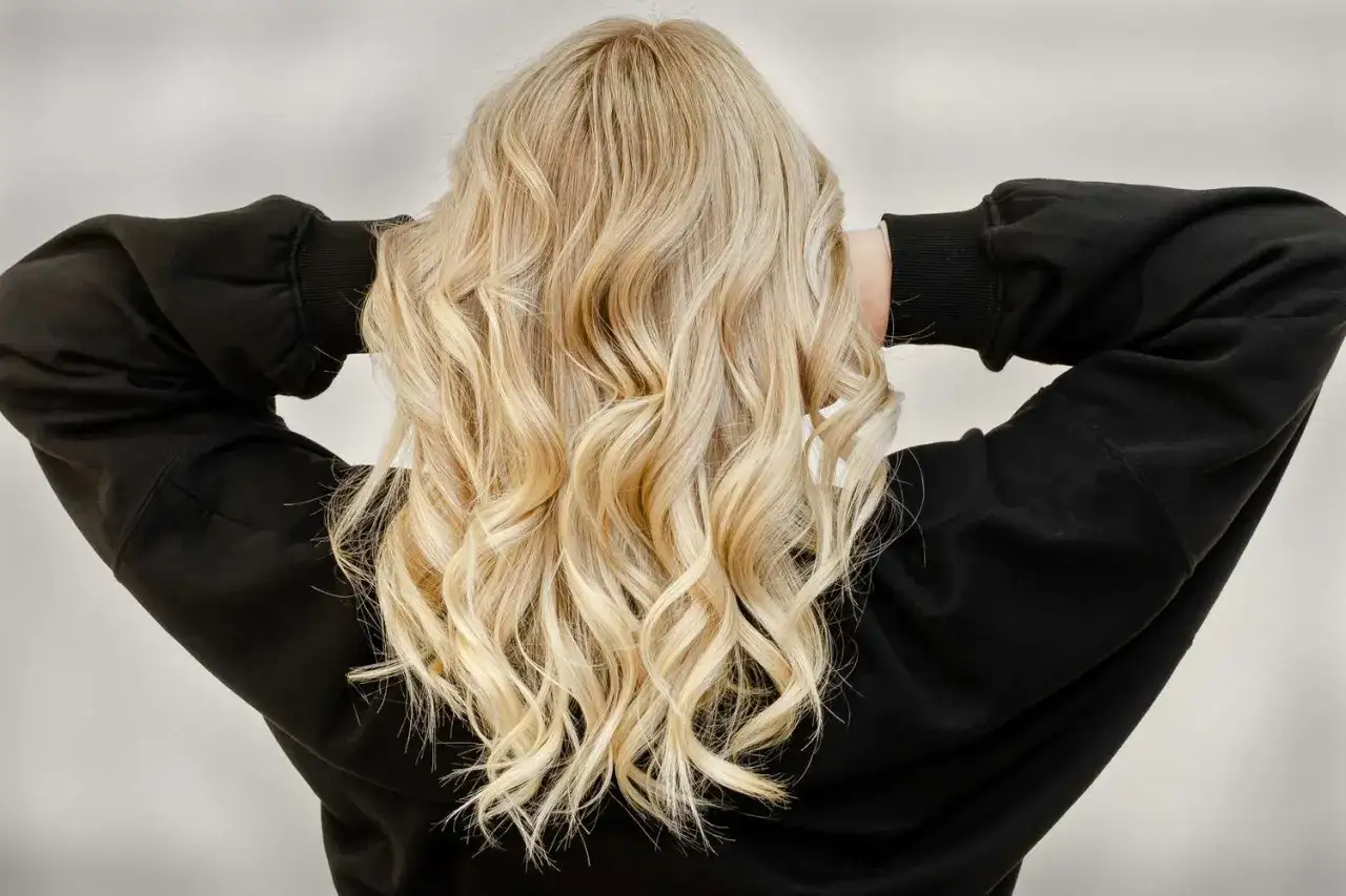 Piękne, falowane blond loki opadają na czarną bluzę.