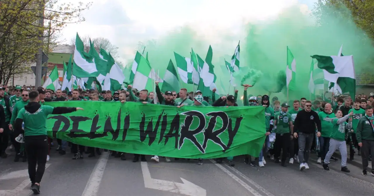 Kibice Radomiaka Radom idą na mecz z Widzewem Łódź, niosąc transparent 