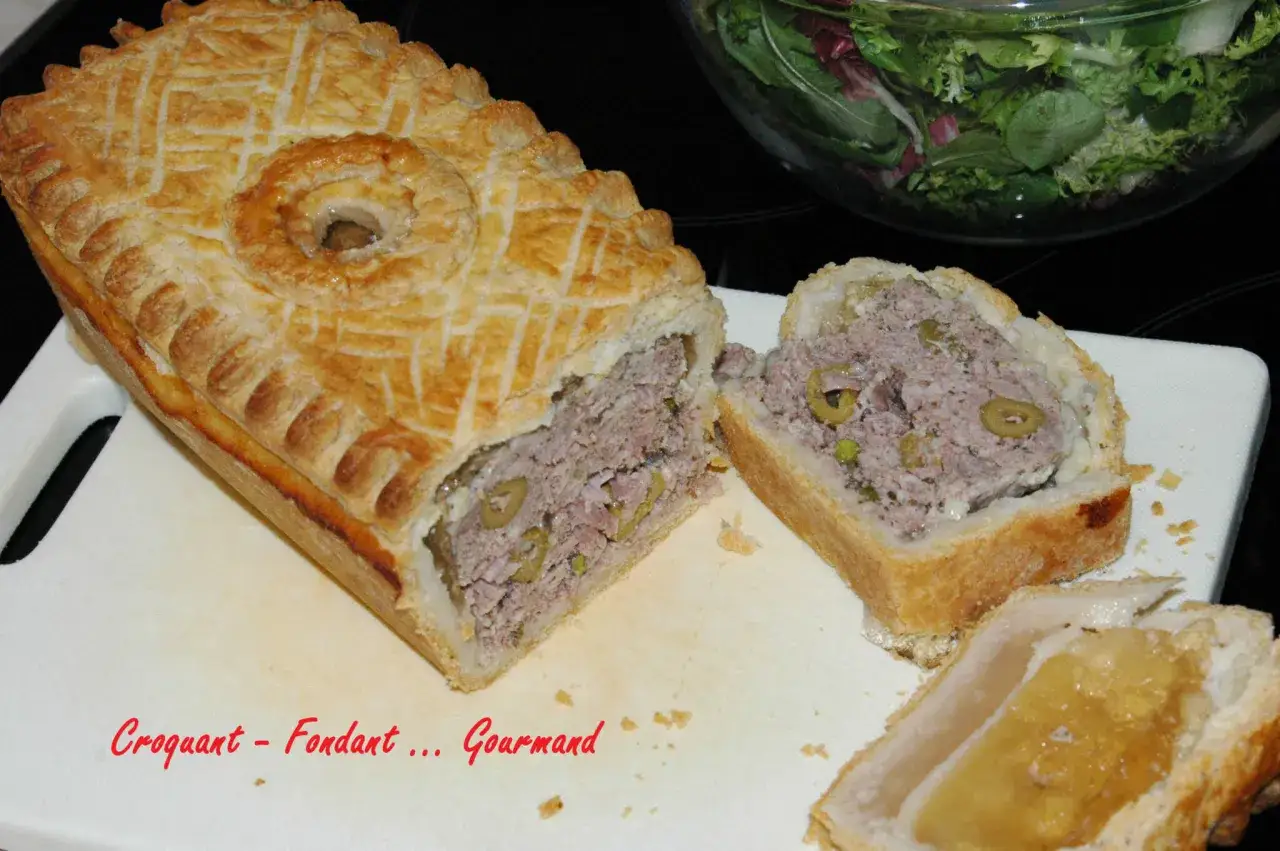 Pâté en croûte aux olives, une tranche coupée révèle sa farce généreuse. Une salade verte est visible en arrière-plan.