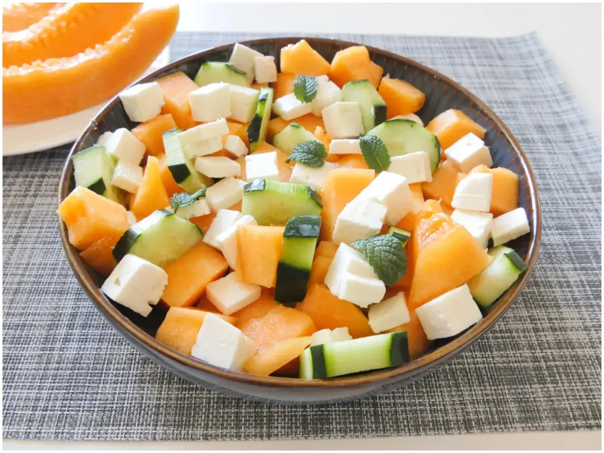 Insalata fresca con cubetti di melone, cetriolo e formaggio bianco, guarnita con foglie di menta.