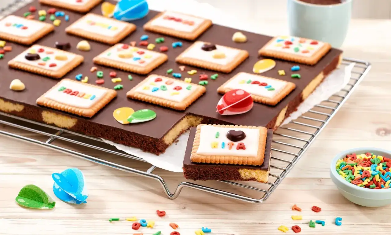 Kreatives Backen mit Kindern im Kindergarten: Bunte Kekse auf Schokoladenkuchen, verziert mit Buchstaben und Figuren.