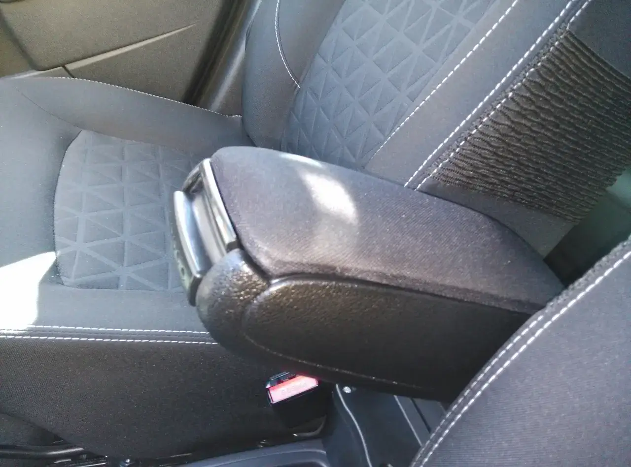 Czarny podłokietnik Dacia Duster, zamontowany między siedzeniami, z widocznym przyciskiem 
