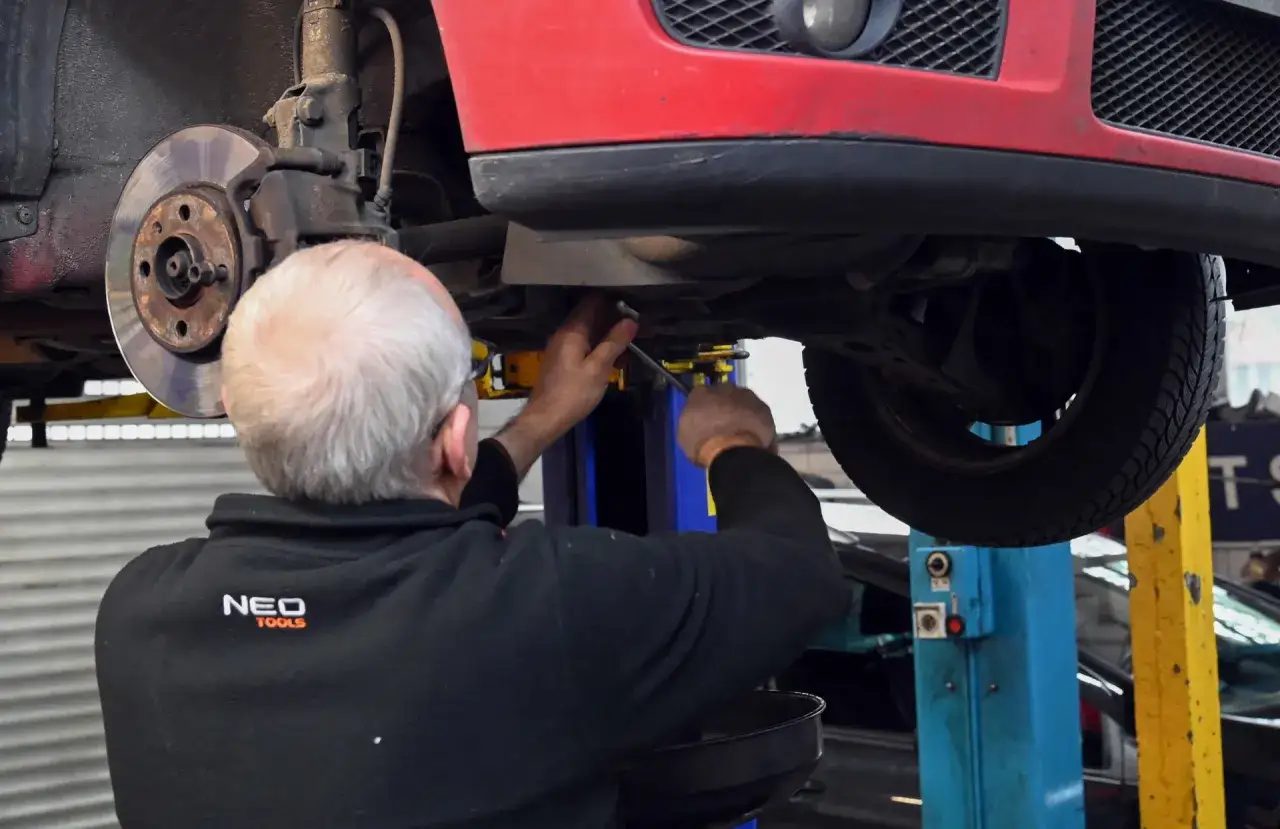 Mechanik wykonuje akcję serwisową Opel Astra H, pracując pod podniesionym czerwonym autem.