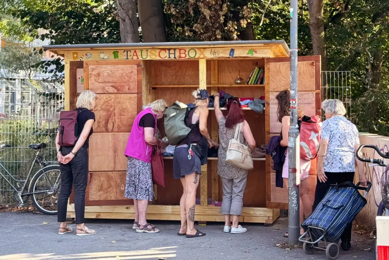 Menschen durchst&ouml;bern eine Tauschbox mit Kleidung und B&uuml;chern, eine Gemeinschaftsaktion, bei der man ohne Geld tauschen kann.