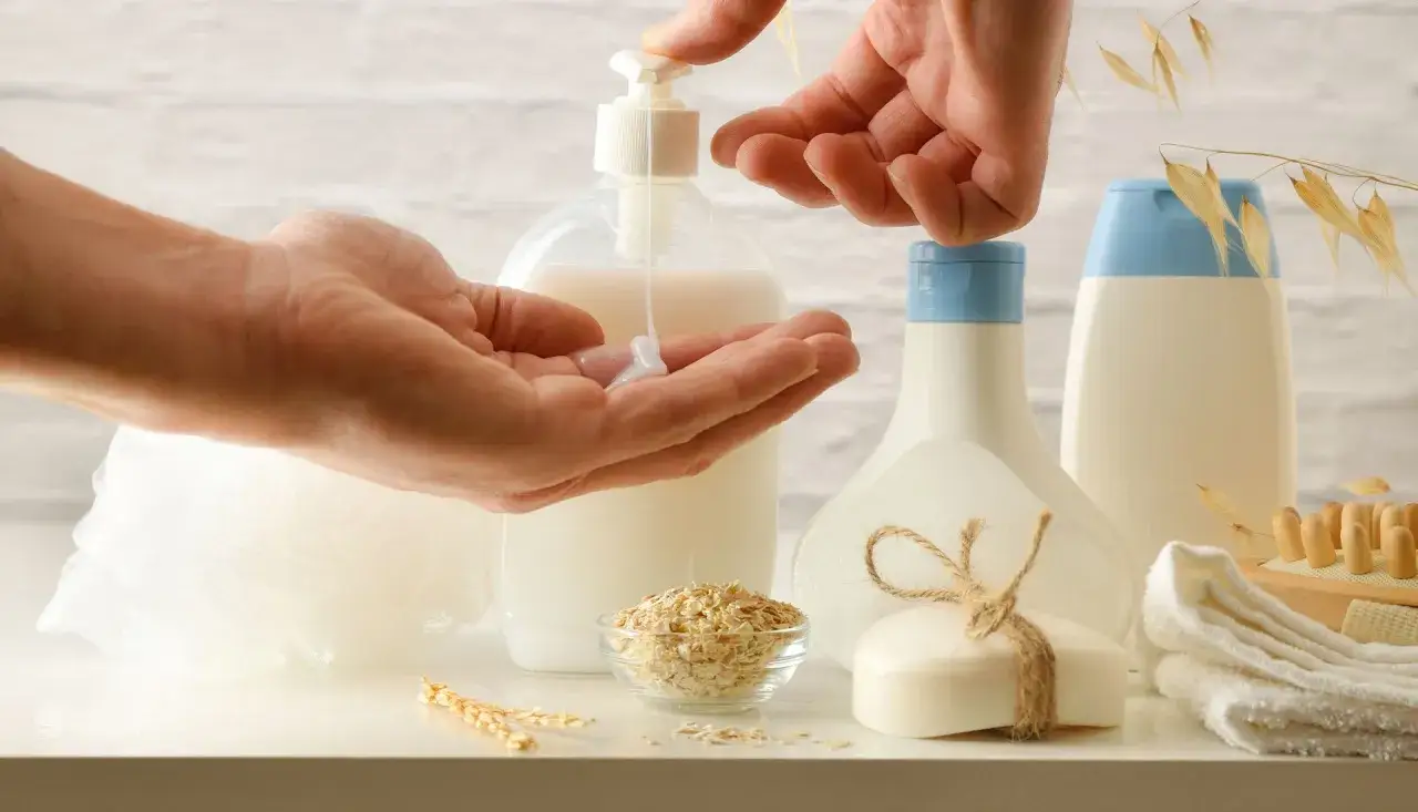 Mani che versano lozione, avena e sapone. Scopri i benefici dell'avena per capelli e pelle.