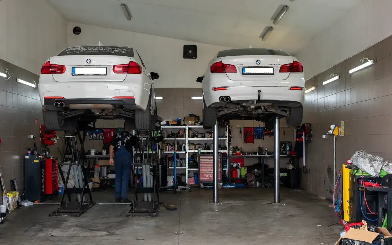 Warsztat samochodowy z dwoma BMW na podnośnikach. Mechanik pracuje przy jednym z aut, diagnozując ewentualne DTC BMW.