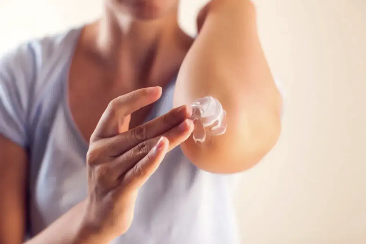Persona aplica crema en sus codos secos para aliviar la sequedad y restaurar la suavidad de la piel.
