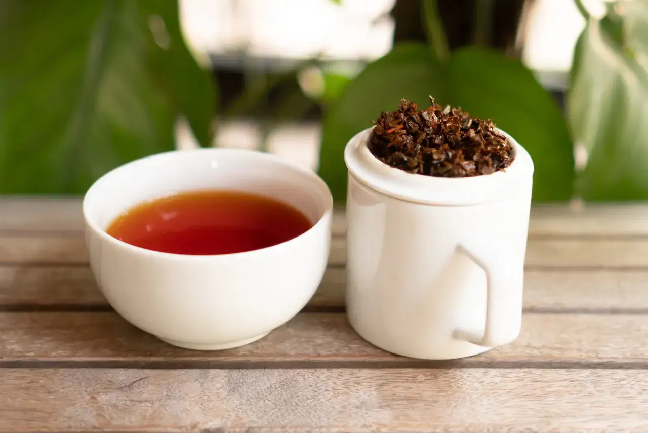 Une tasse de thé ambré et une tasse remplie de feuilles de thé séchées. Le thé ceylan bienfait pour la santé.