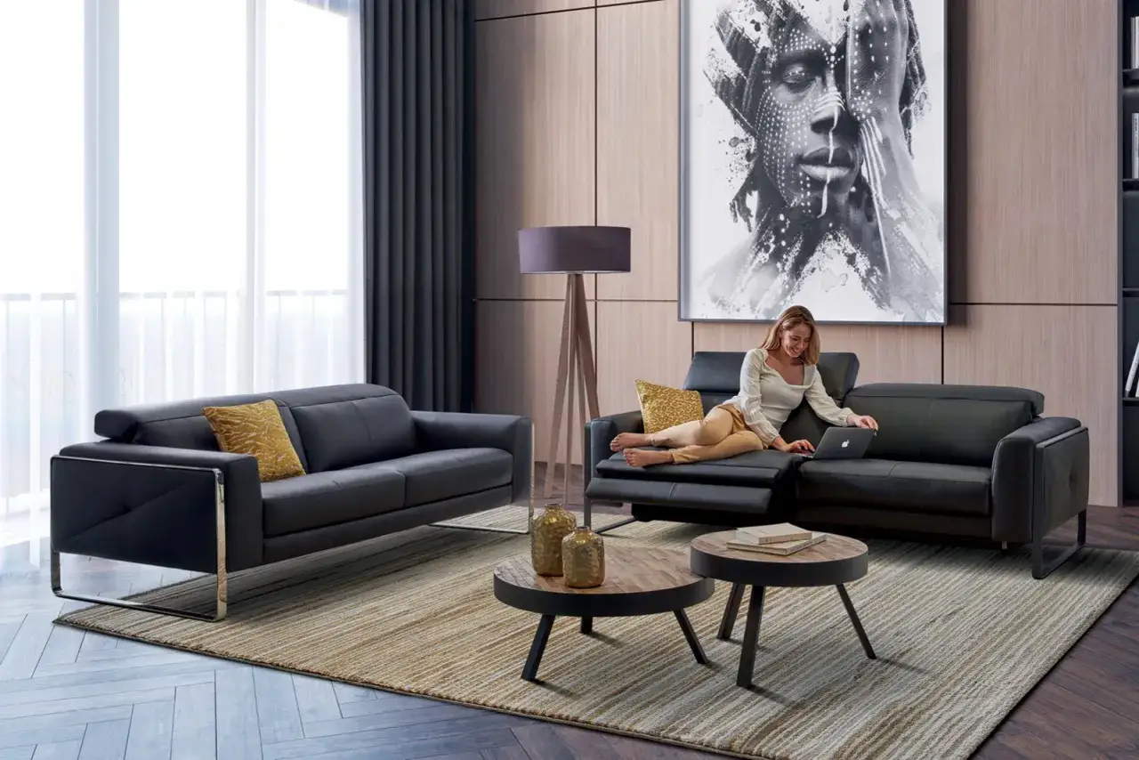 Idée déco salon : un canapé noir moderne, coussins jaunes, table basse et une femme sur son ordinateur.