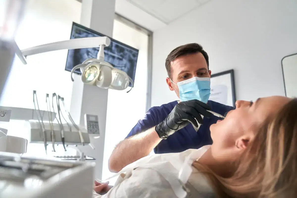 Dentysta w masce bada zęby pacjentki. Może to być etap przygotowania do szynowania zębów na NFZ.