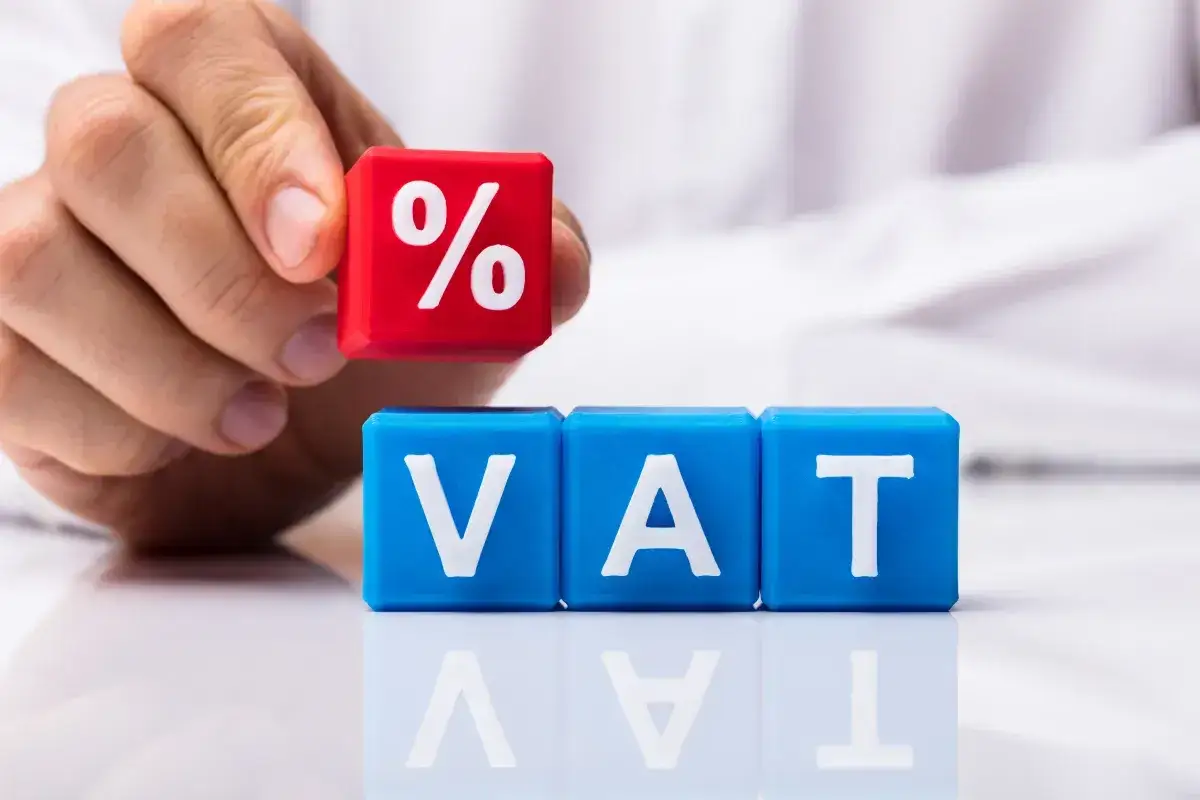 Ręka układa kostkę z symbolem procentu na kostkach z napisem VAT. Zmiana stawek VAT.