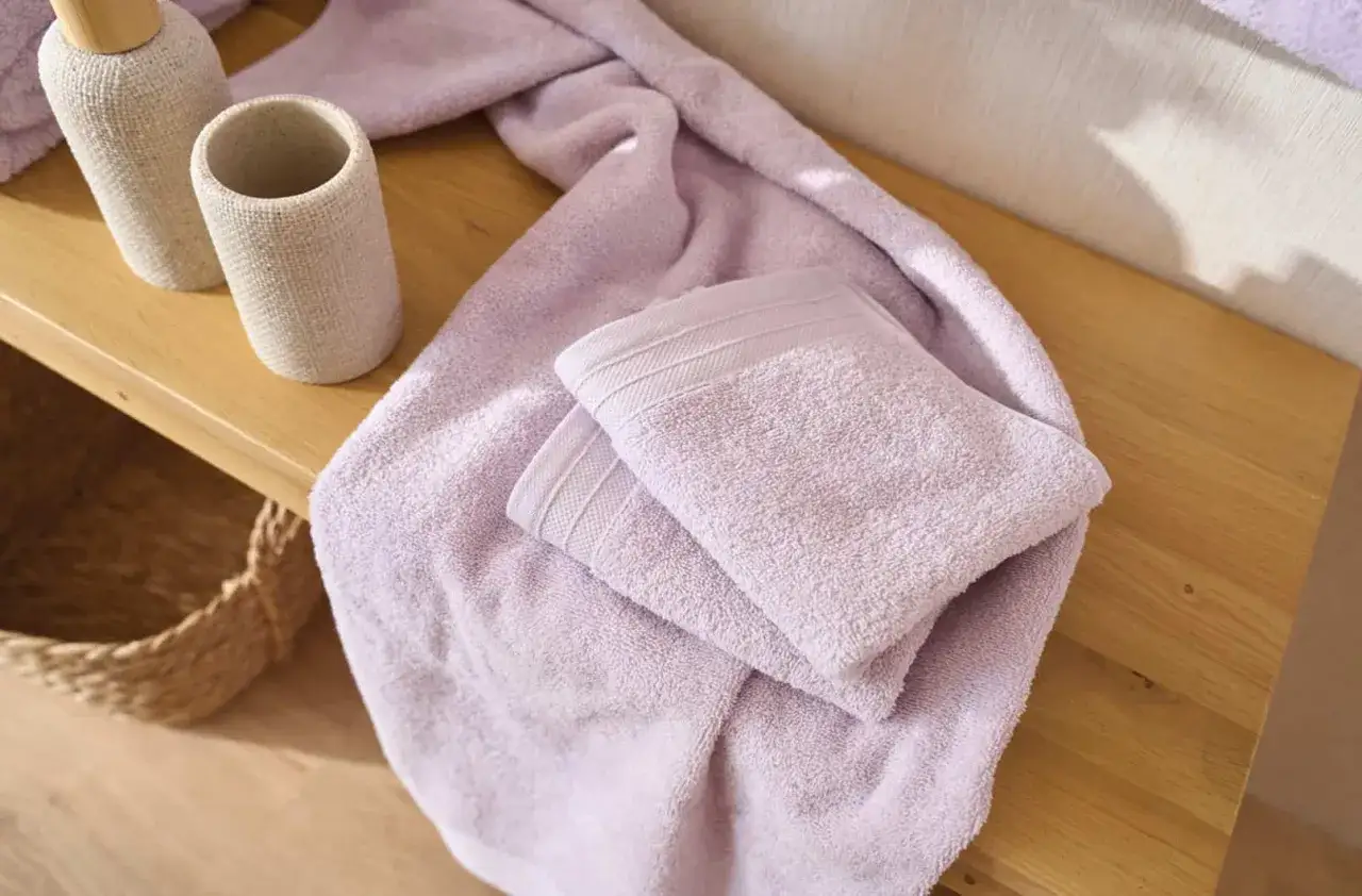 Variedad de tipos de toallas de ba&ntilde;o en color lavanda, apiladas sobre una superficie de madera.