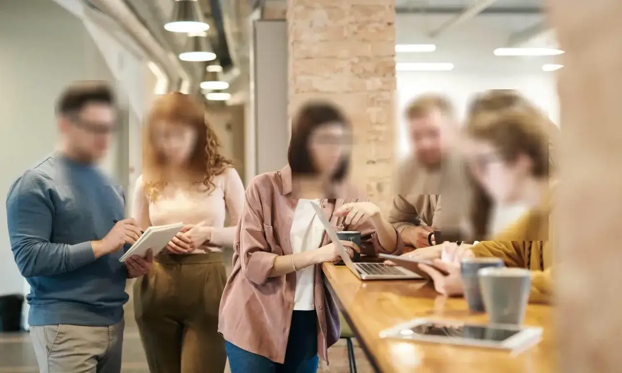 Zespół pracuje nad projektem, a twarze są zamaskowane. Widać notatki i laptop, co sugeruje, że to sposób, jak zamazać coś na zdjęciu.