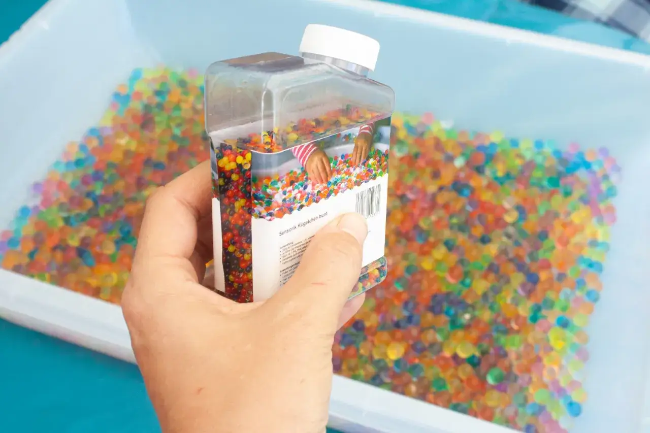 Bunte Wasserperlen in einer Hand, bereit f&uuml;r sensorische Spielideen.