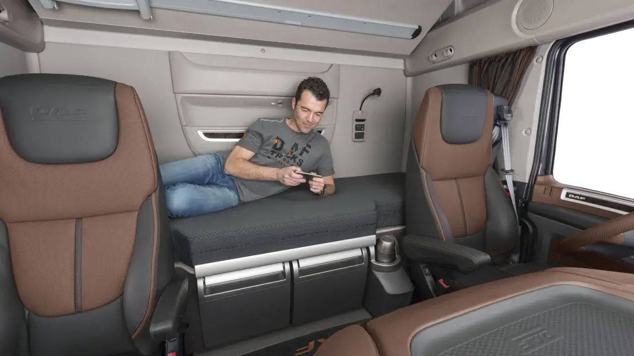 Mężczyzna relaksuje się na łóżku w kabinie DAF XF 105, przeglądając telefon.