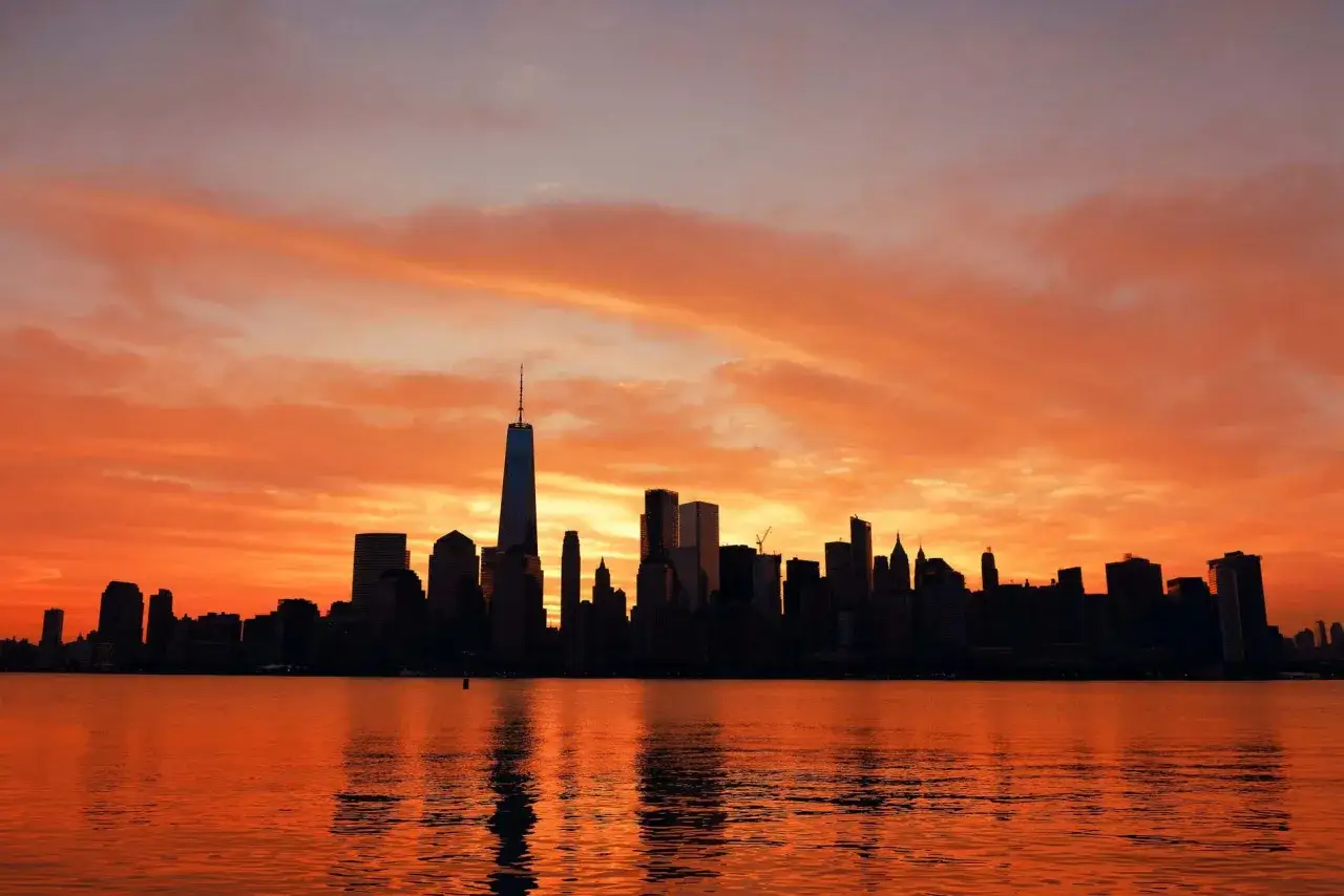 Fiery sunset over the NYC skyline, a perfect backdrop for 36 hours in NYC. The water reflects the vibrant orange and purple clouds.