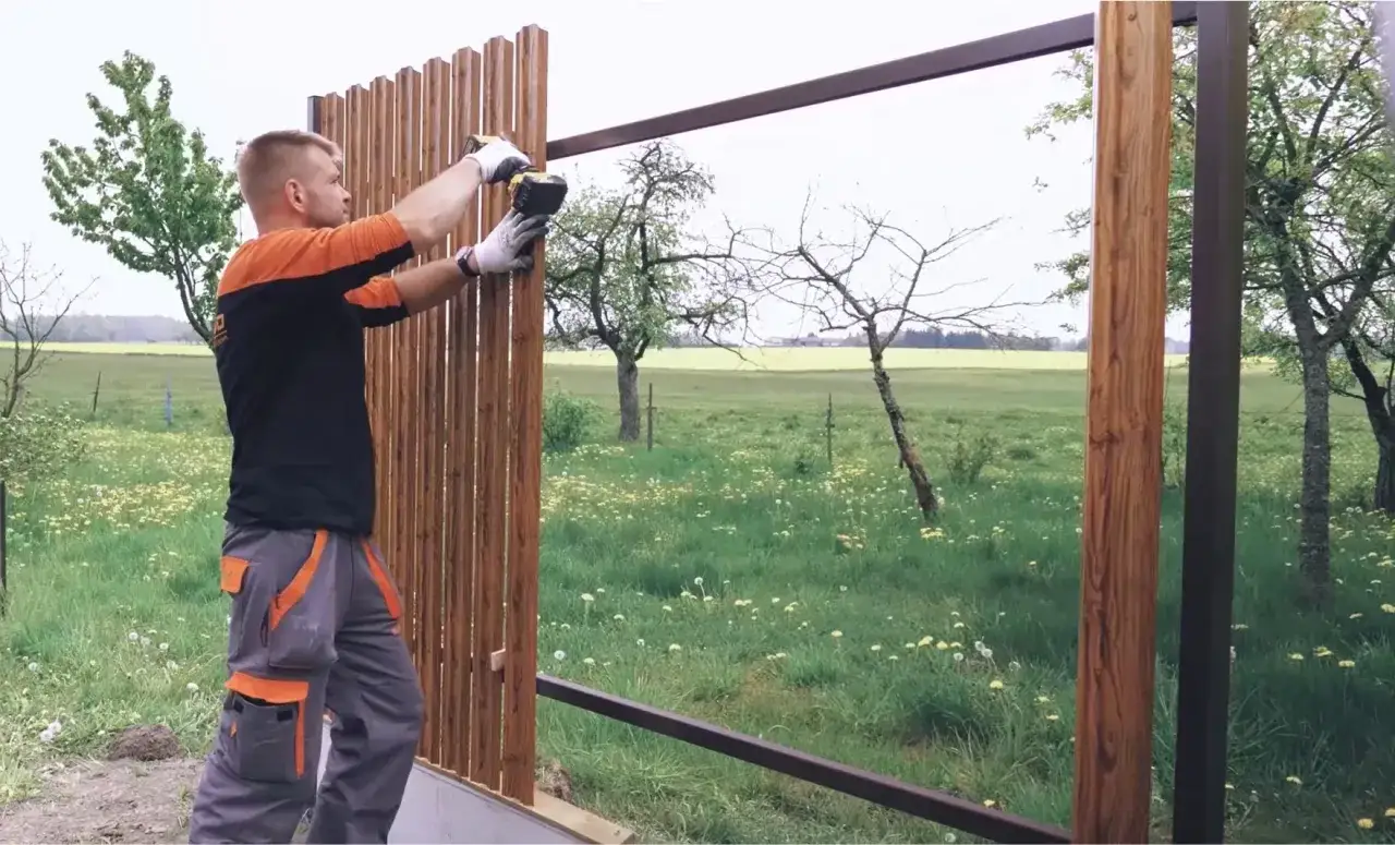 Mężczyzna montuje drewniane sztachety, tworząc płot. Widać, ile sztachet na metr jest potrzebne do budowy.