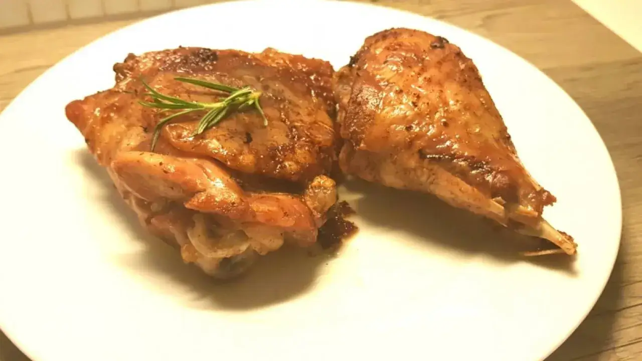 Due pezzi succulenti di fesa di tacchino arrosto, guarniti con rosmarino fresco, su un piatto bianco.