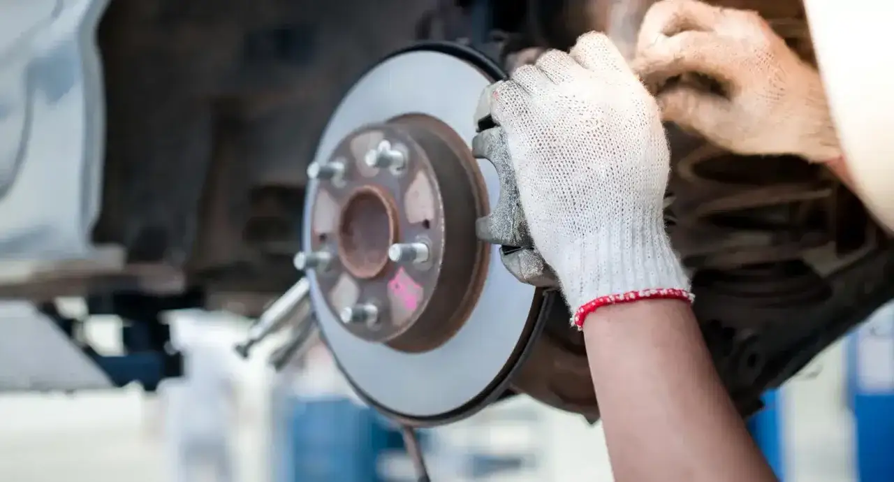 Ein Mechaniker mit Handschuhen montiert eine Bremsscheibe. So sieht eine Bremse aus, wenn sie repariert wird.