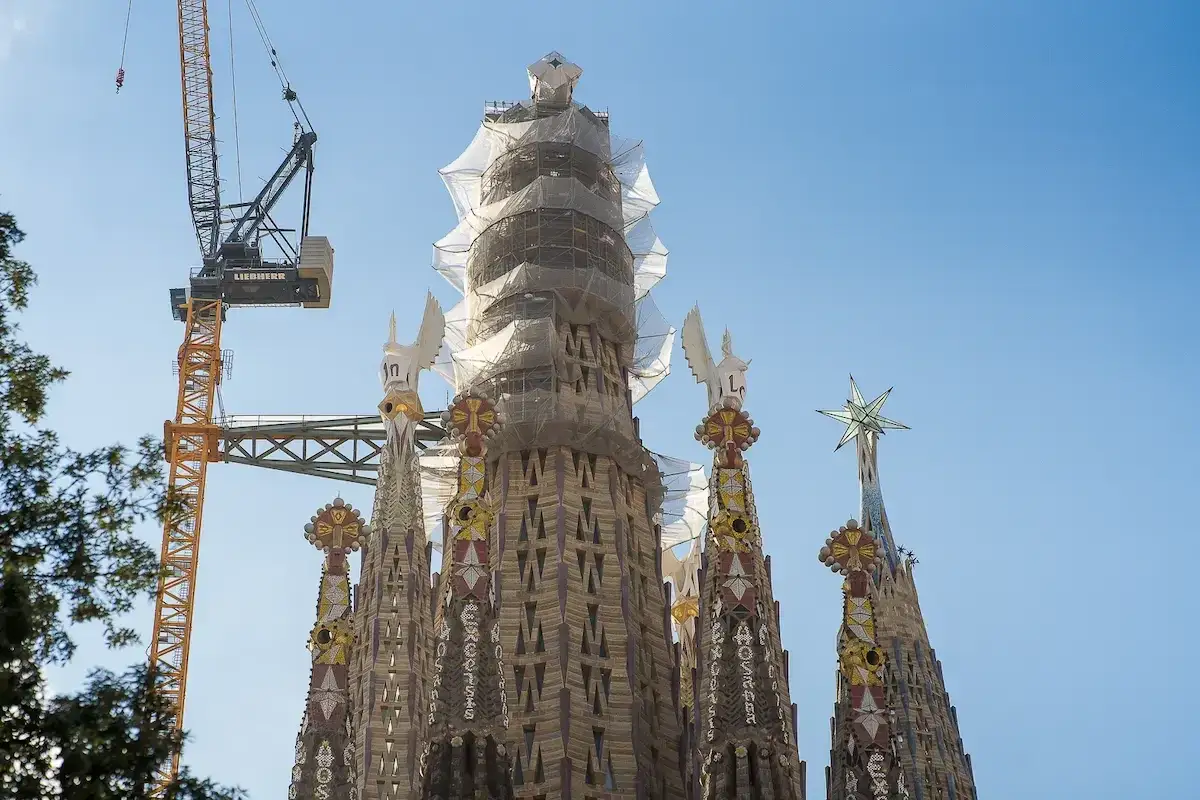 La Sagrada Familia, en plein temps de construction, avec une grue Liebherr dominant le ciel bleu. Les tours sont encore drap&eacute;es de b&acirc;ches.
