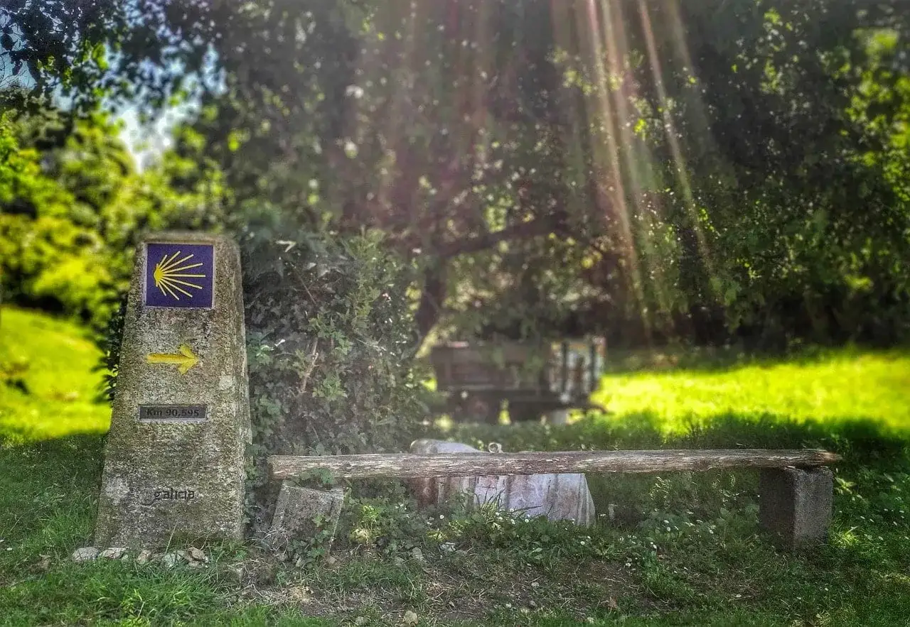 Moj&oacute;n del Camino de Santiago desde Ferrol, con flecha amarilla y vieira. Banco r&uacute;stico invita a descansar.
