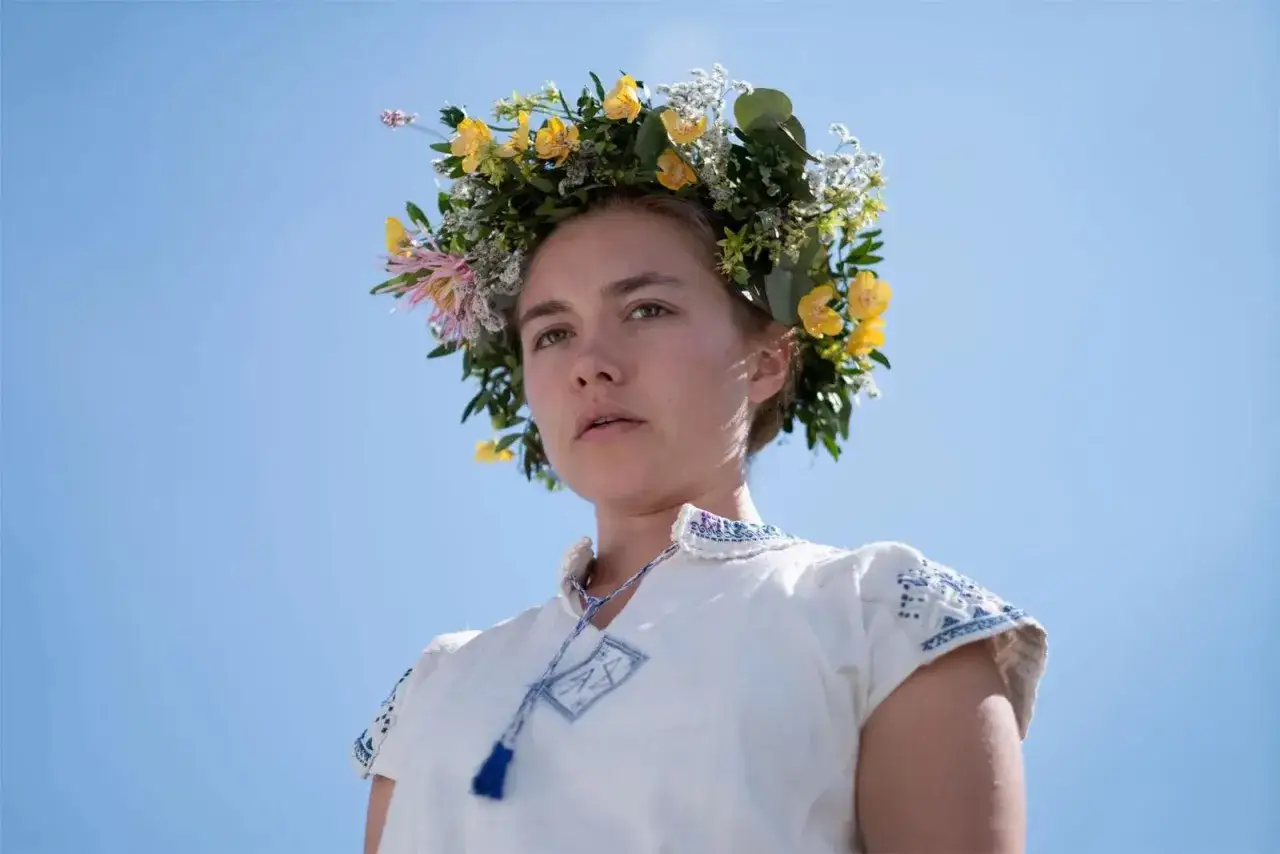 En kvinna med blomsterkrans bär en broderad klänning. Hon är en del av rollistan i midsommarfilmen.