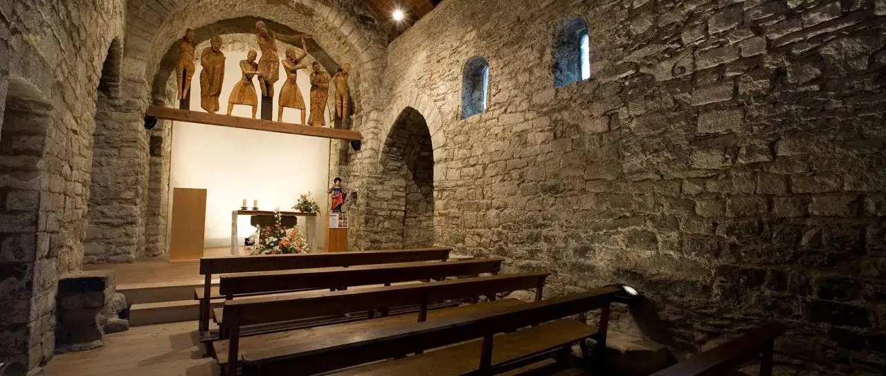 Interior de una de las iglesias rom&aacute;nicas del Vall de Bo&iacute;, con bancos de madera y un altar decorado.