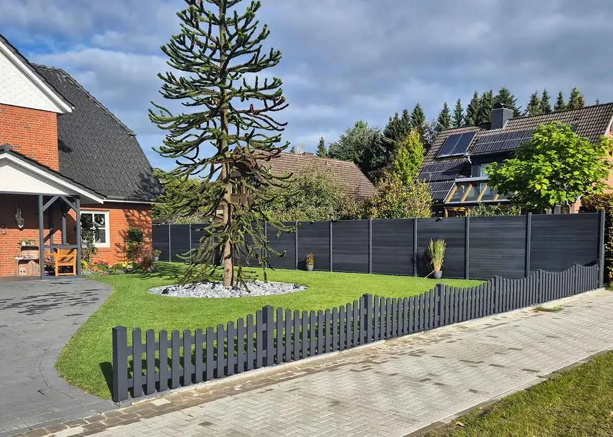 Moderne gartenzaun ideen: Ein niedriger, grauer Lattenzaun grenzt den gepflegten Rasen ab. Dahinter sch&uuml;tzt ein dunkler, blickdichter Zaun das Grundst&uuml;ck.