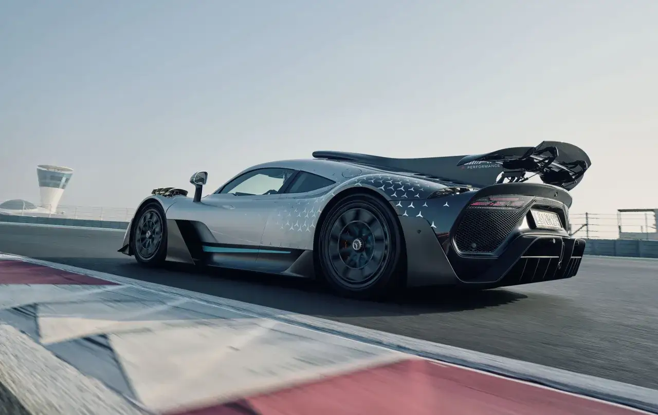 Srebrny Mercedes-AMG ONE z czarnym skrzydłem i wzorem gwiazd pędzi po torze wyścigowym.