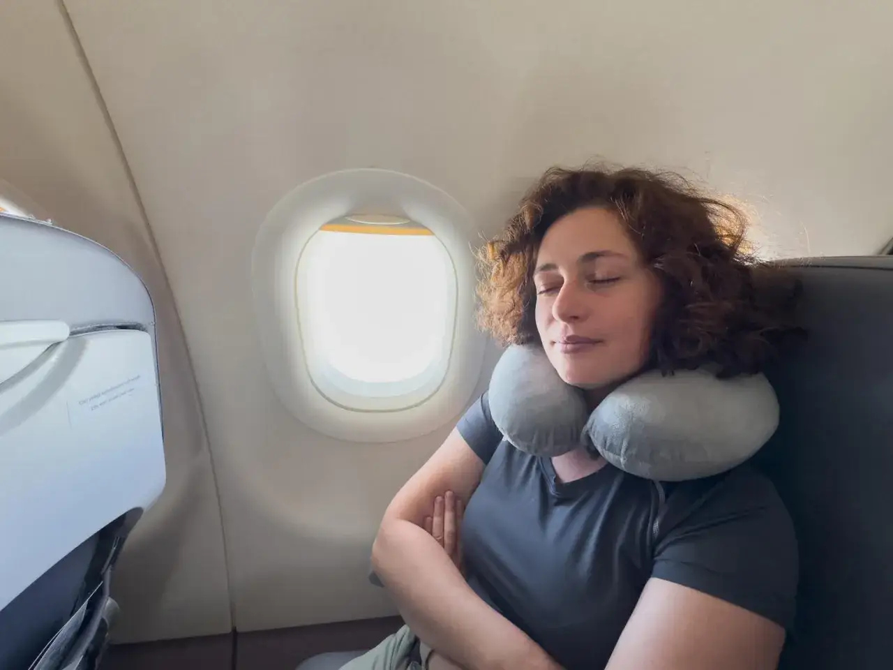 Frau schläft im Flugzeug mit Nackenkissen. Ein gutes Mittel, was tun gegen Flugangst: einfach entspannen und schlafen.