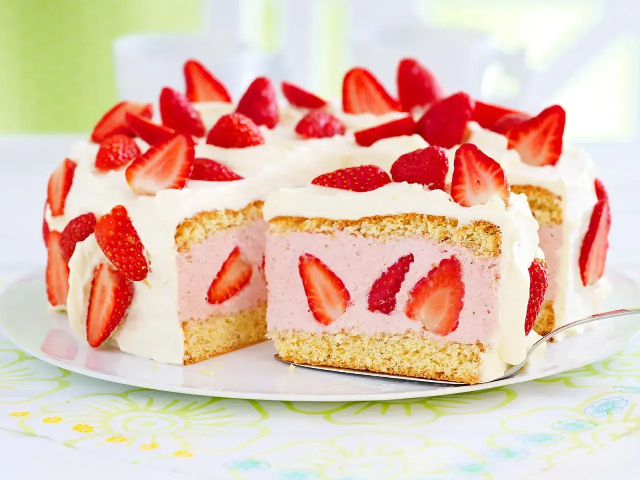 Eine k&ouml;stliche Torte mit Erdbeeren, &uuml;ppig mit Sahne und frischen Fr&uuml;chten dekoriert. Ein St&uuml;ck wurde bereits angeschnitten, um die saftige F&uuml;llung zu enth&uuml;llen.