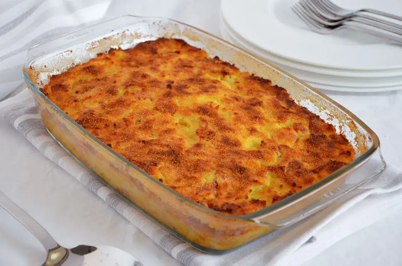 Un invitante gateau di patate dorato e croccante in una pirofila di vetro, pronto per essere servito.