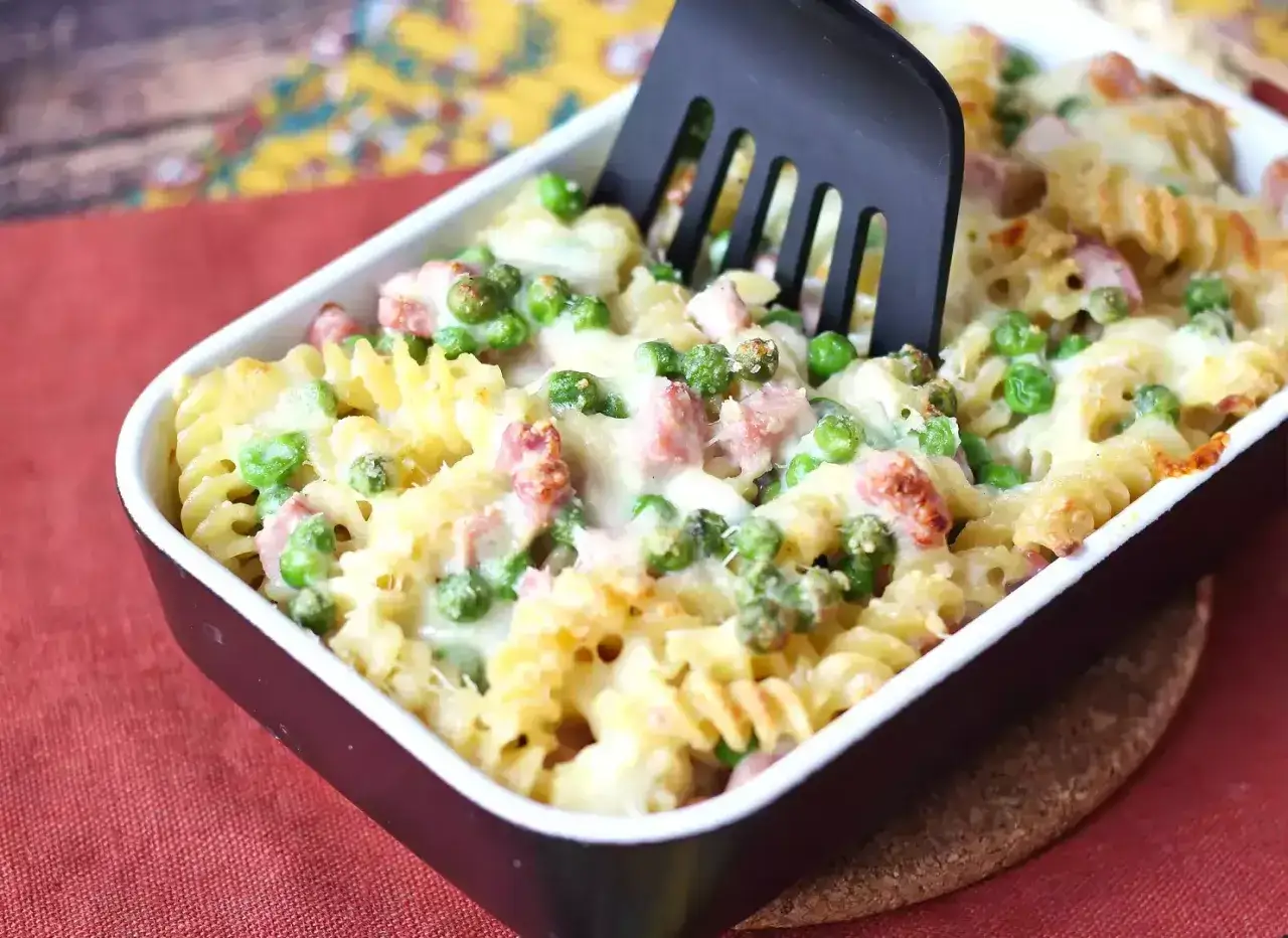 Un invitante piatto di pasta al forno con piselli e prosciutto, pronto per essere servito.