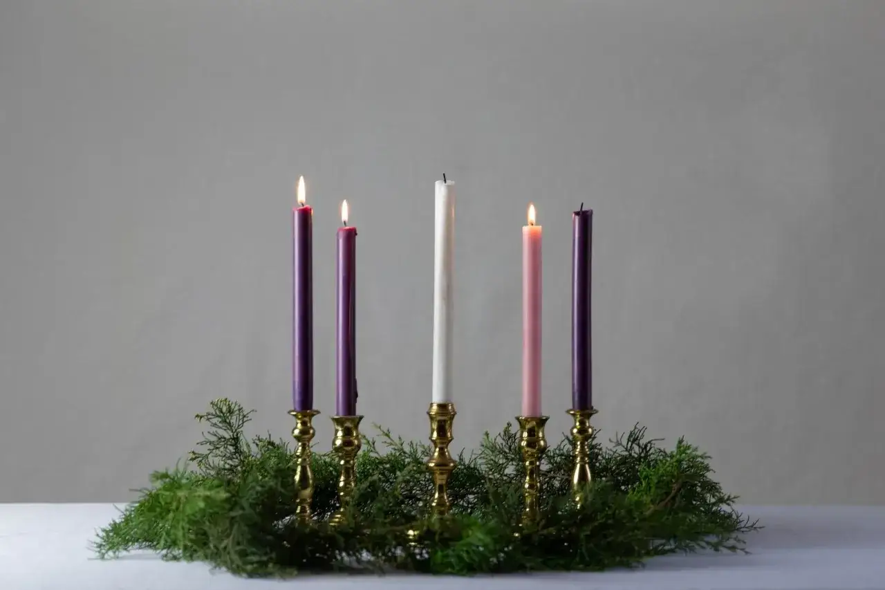 Five candles in brass holders, with greenery, mark the advent 3rd Sunday. Two purple, one pink, and one white candle are lit.
