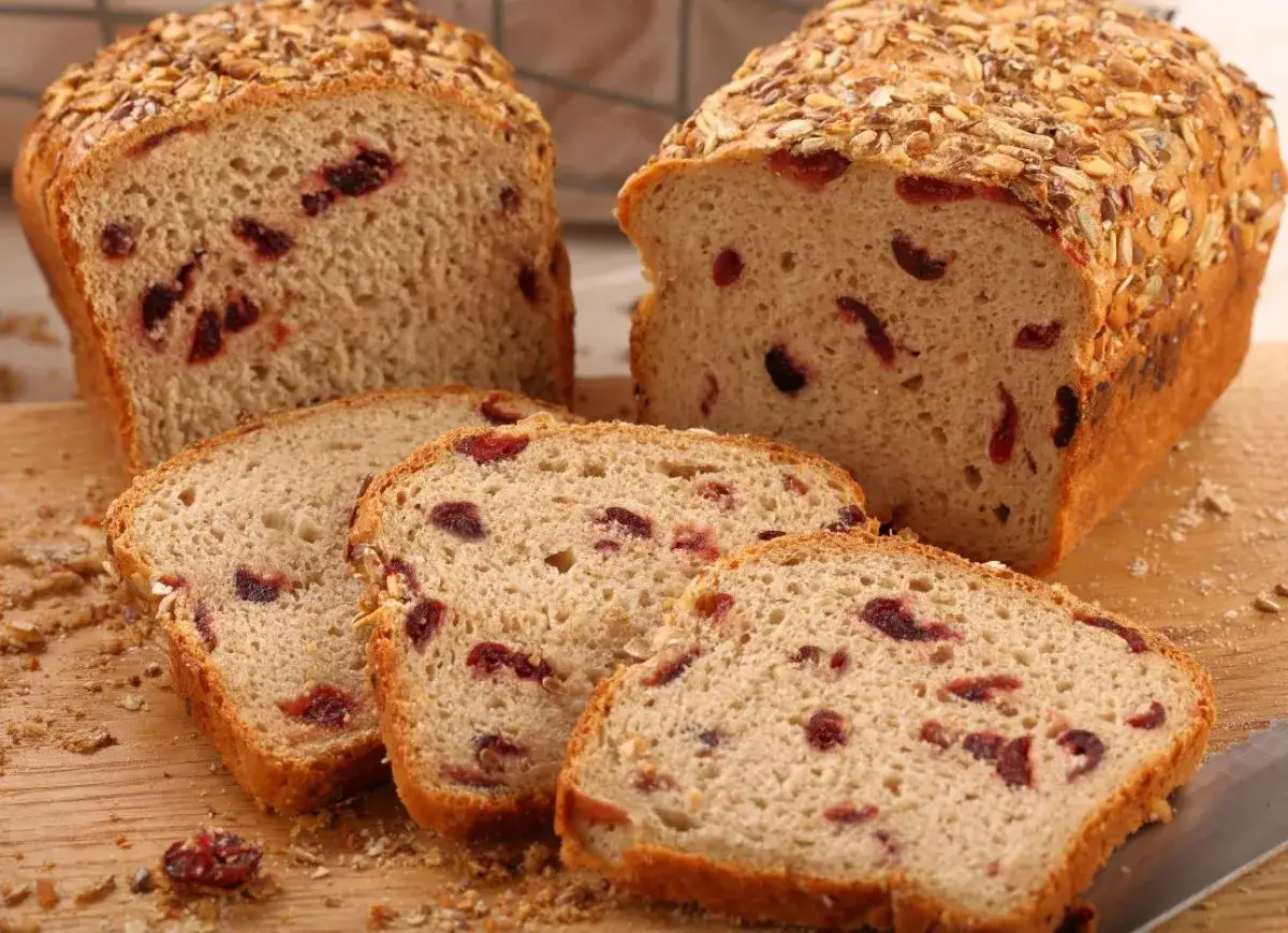 Dwa bochenki chleba z żurawiną i ziarnami na wierzchu, jeden pokrojony na kromki, leżą na desce.