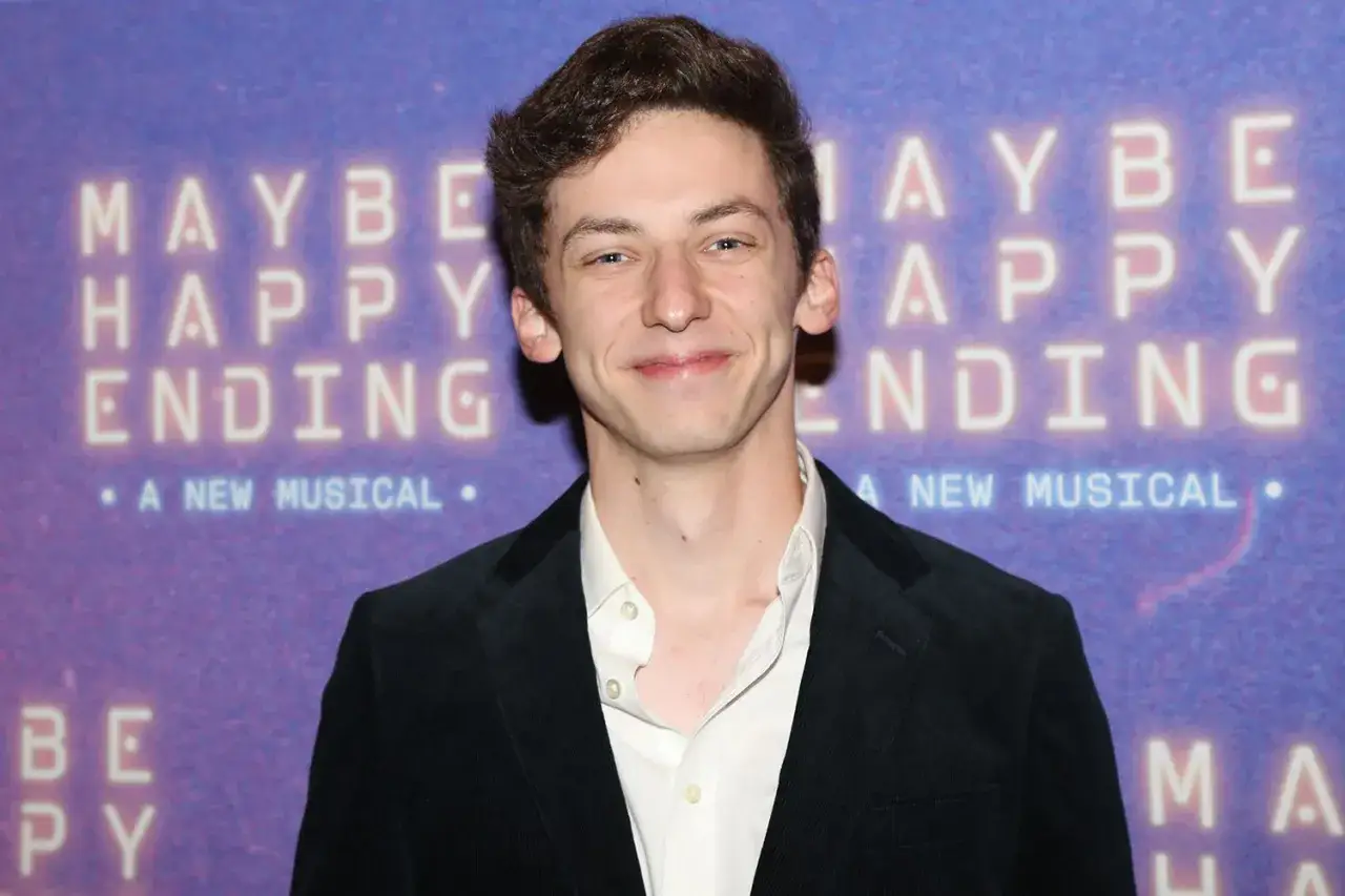 Andrew Barth Feldman lächelt vor einem Banner für das Musical