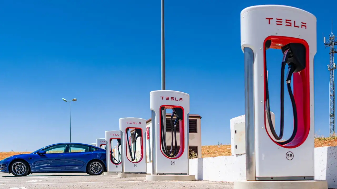 Niebieski Tesla na stacji ładowania. Czy Tesla potrzebuje benzyny? Absolutnie nie, bo ładuje się prądem!