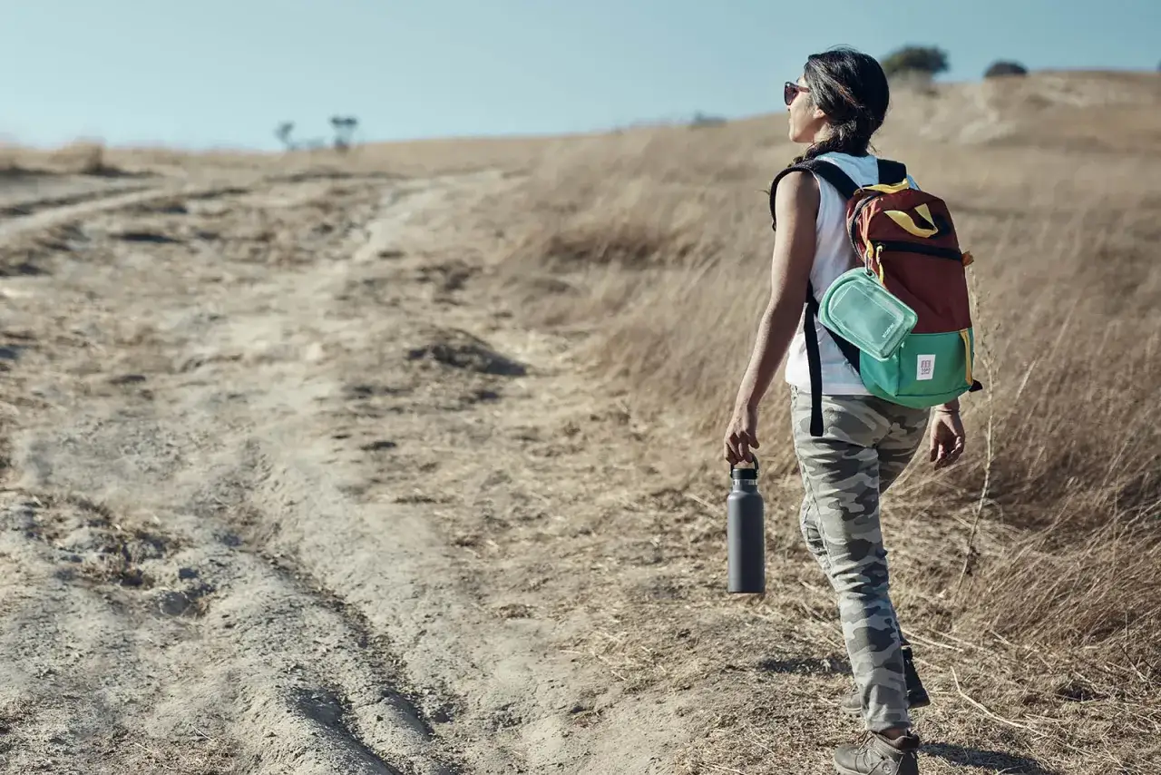 Frau wandert auf staubigem Pfad, Rucksack und Wasserflasche dabei. Guter Kalorienverbrauch beim Wandern in der Natur.