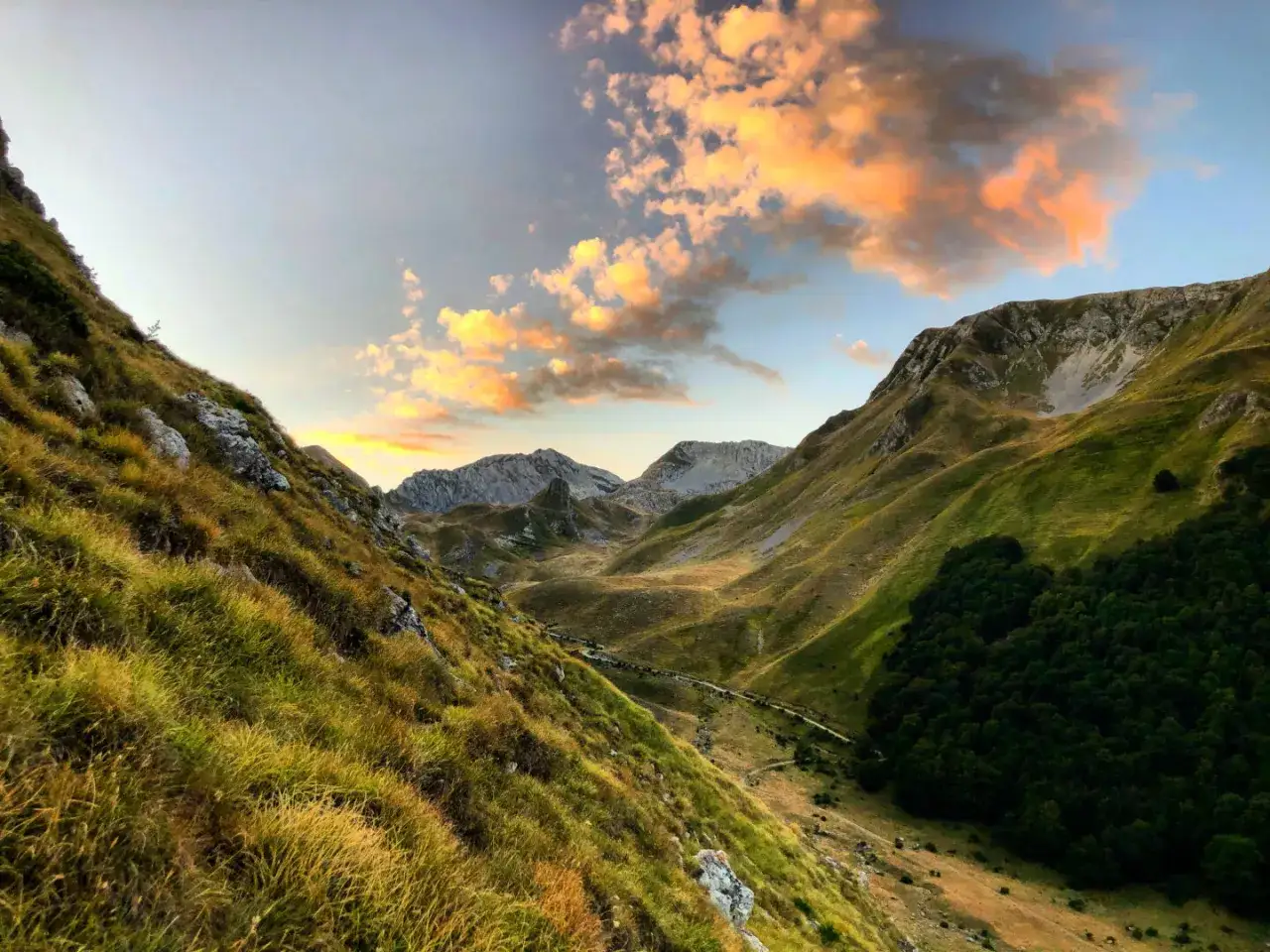 Valli verdi e pendii erbosi sotto un cielo infuocato al tramonto, con le cime del monte Corvo che si stagliano all'orizzonte.