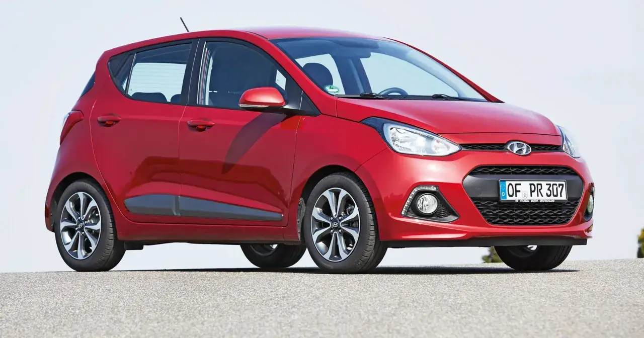 Czerwony Hyundai i10 z niemieckimi tablicami rejestracyjnymi stoi na szarej nawierzchni.