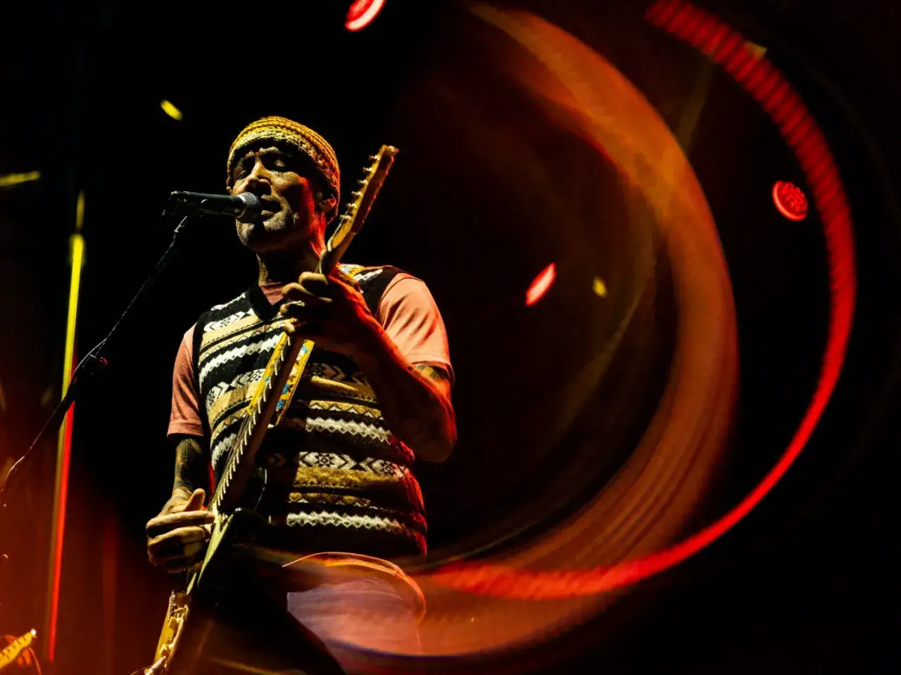 Ben Harper, le musicien, joue de la guitare sur sc&egrave;ne, baign&eacute; de lumi&egrave;res chaudes et tourbillonnantes.