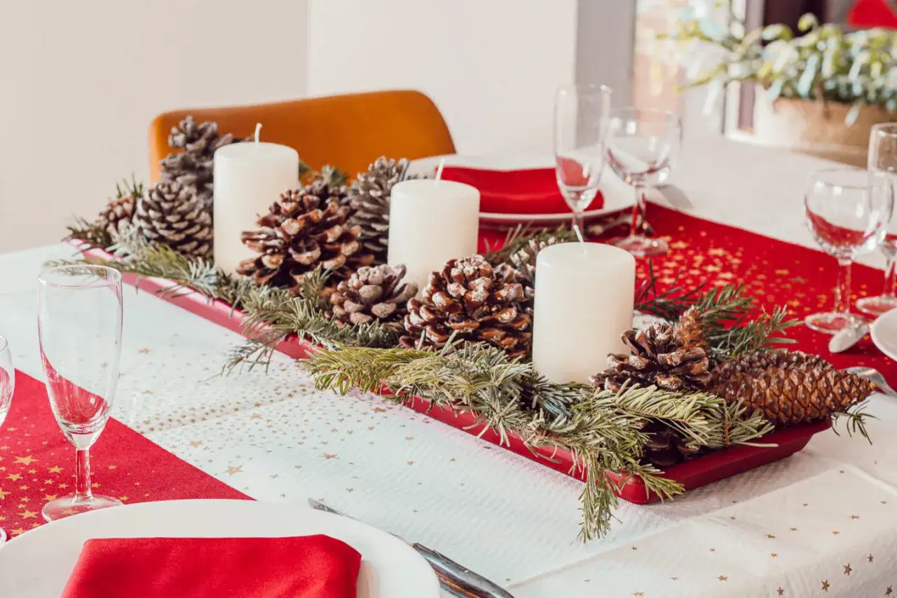 Un chemin de table No&euml;l &agrave; faire soi-m&ecirc;me orn&eacute; de pommes de pin, de branches de sapin et de bougies blanches sur une table dress&eacute;e.