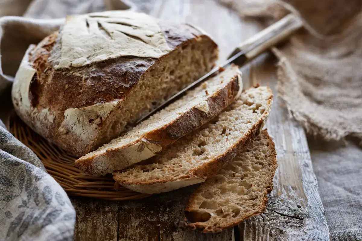 Pane fatto in casa con lievito di birra, tagliato a fette su un tagliere di legno. La crosta &egrave; dorata e croccante, l'interno morbido e alveolato.