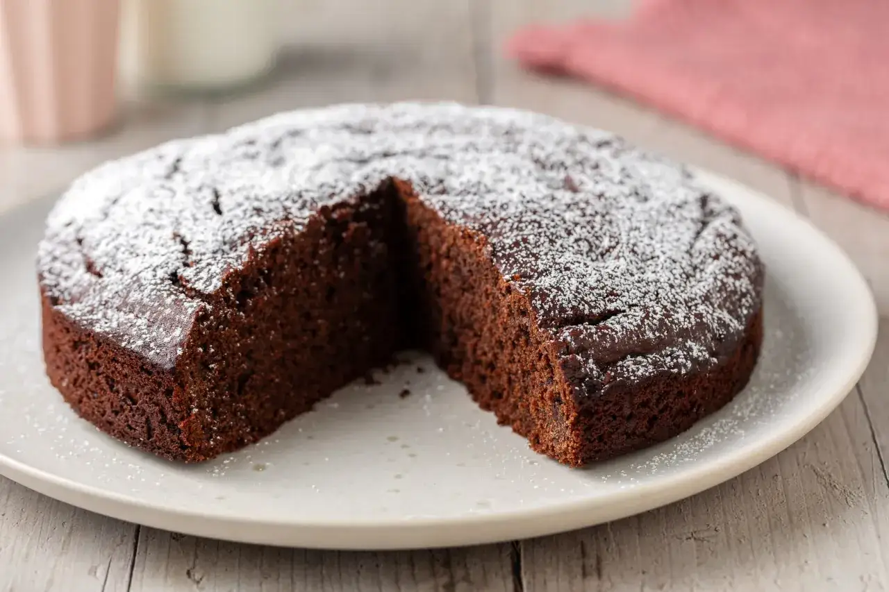 Una deliziosa torta al cioccolato senza burro, spolverata di zucchero a velo, su un piatto bianco.
