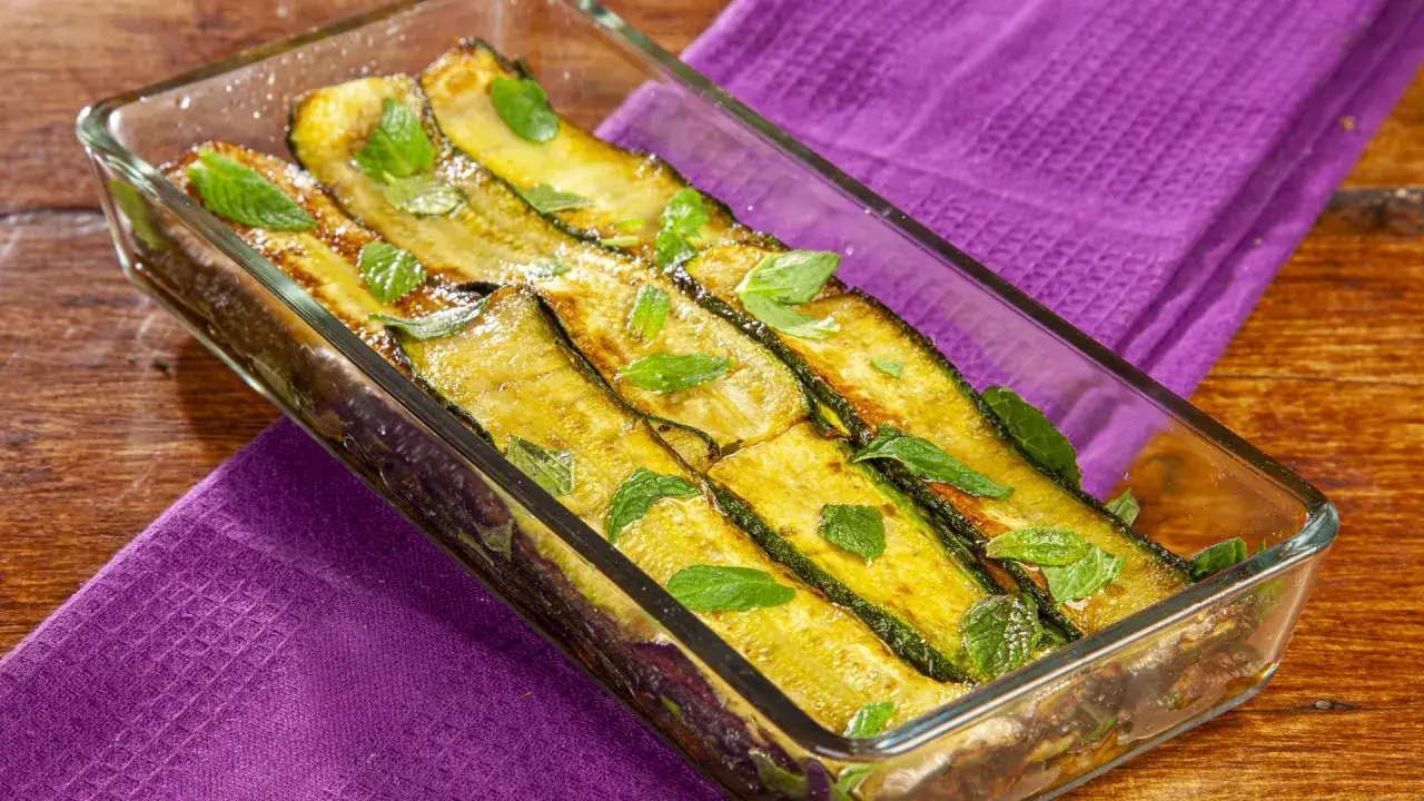 Zucchine alla scapece ricetta napoletana in una pirofila di vetro, guarnite con foglie di menta fresca.