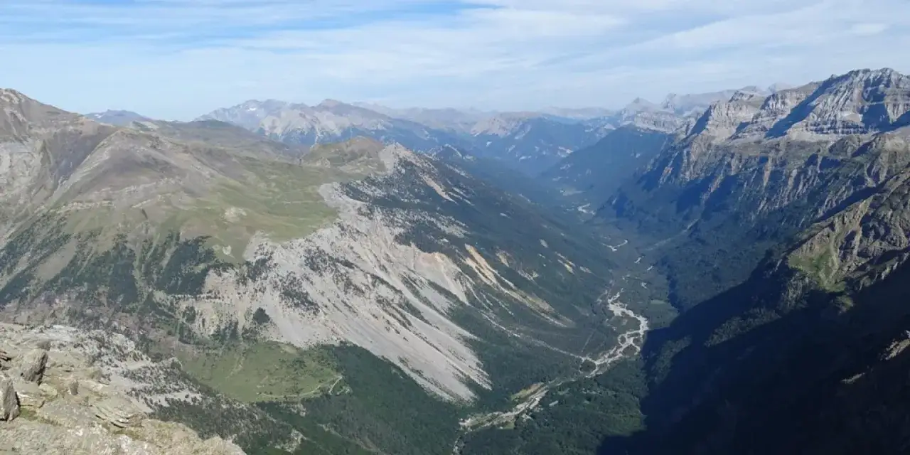 Vue panoramique des **llanos de la Larri**, une vallée verdoyante bordée de montagnes escarpées sous un ciel bleu.