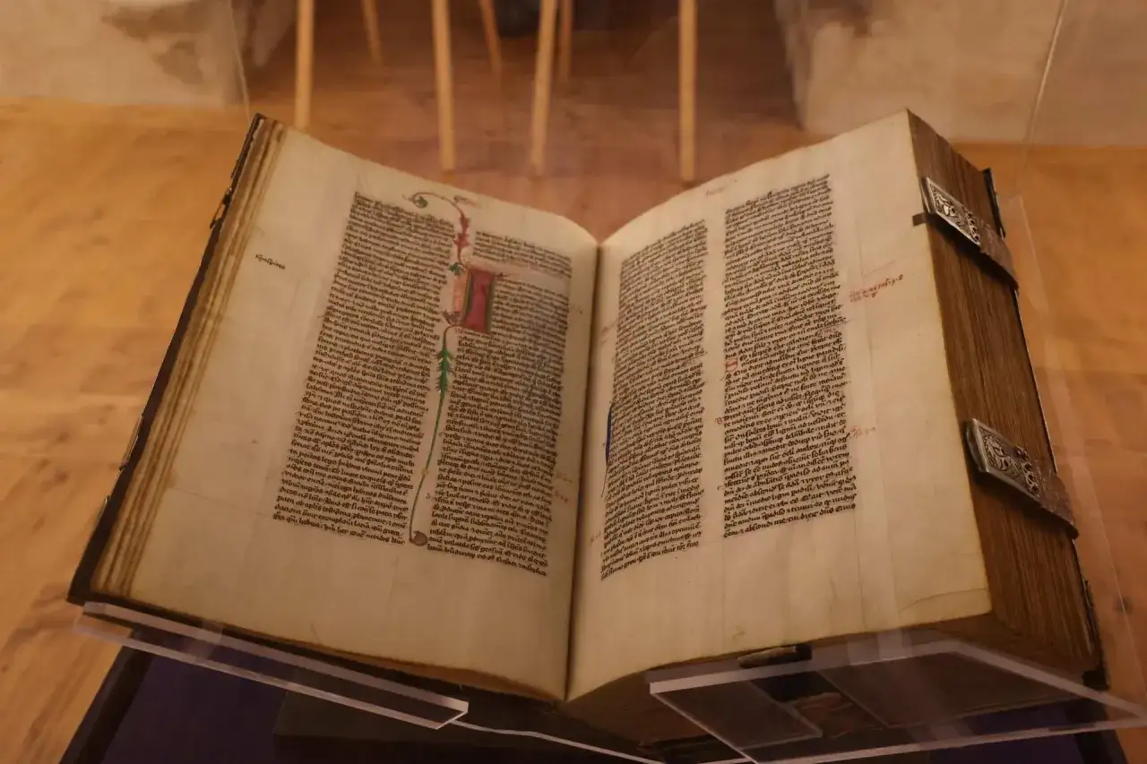 Altes, aufgeschlagenes Buch mit handgeschriebenen Texten und Illustrationen. Eine Frage, die sich viele stellen: wer hat die Bibel geschrieben?