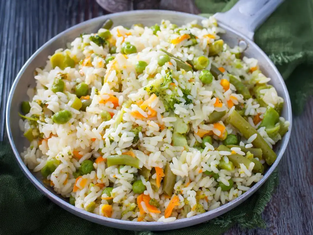 Arroz blanco con verduras, una mezcla colorida de br&oacute;coli, zanahoria y guisantes, servido en una sart&eacute;n.