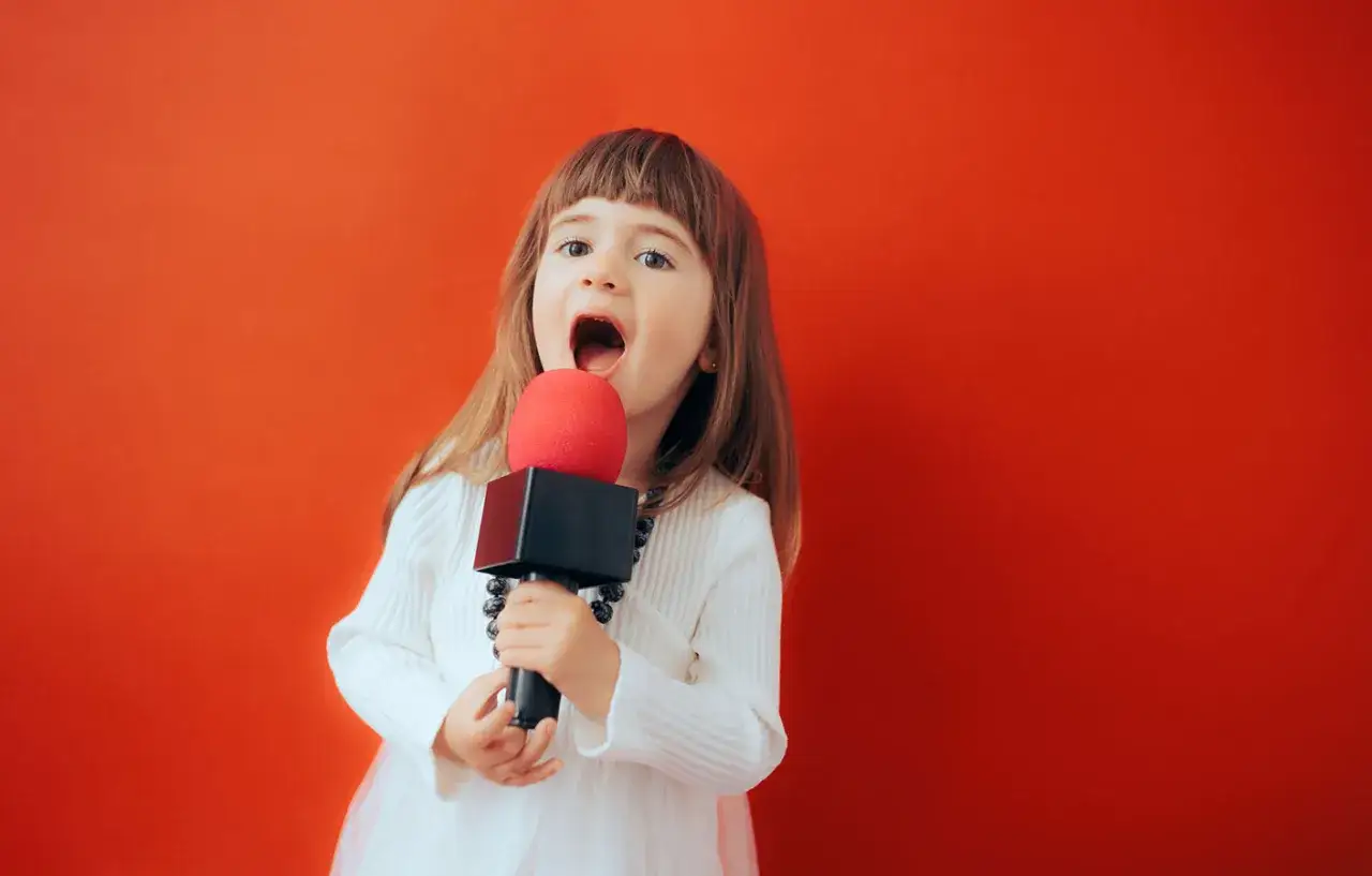 Kleines M&auml;dchen mit Mikrofon, das singt. M&ouml;gliche Ursachen f&uuml;r Stottern sind vielf&auml;ltig und komplex.